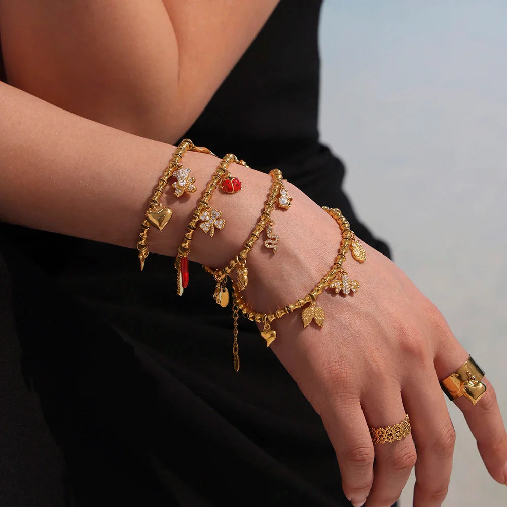 Person’s arm with gold charm bracelets and rings featuring cubic zircon geometric pendants