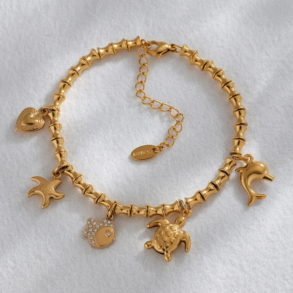 Gold-toned charm bracelet with marine animal and heart charms, featuring cubic zircon geometric pendant