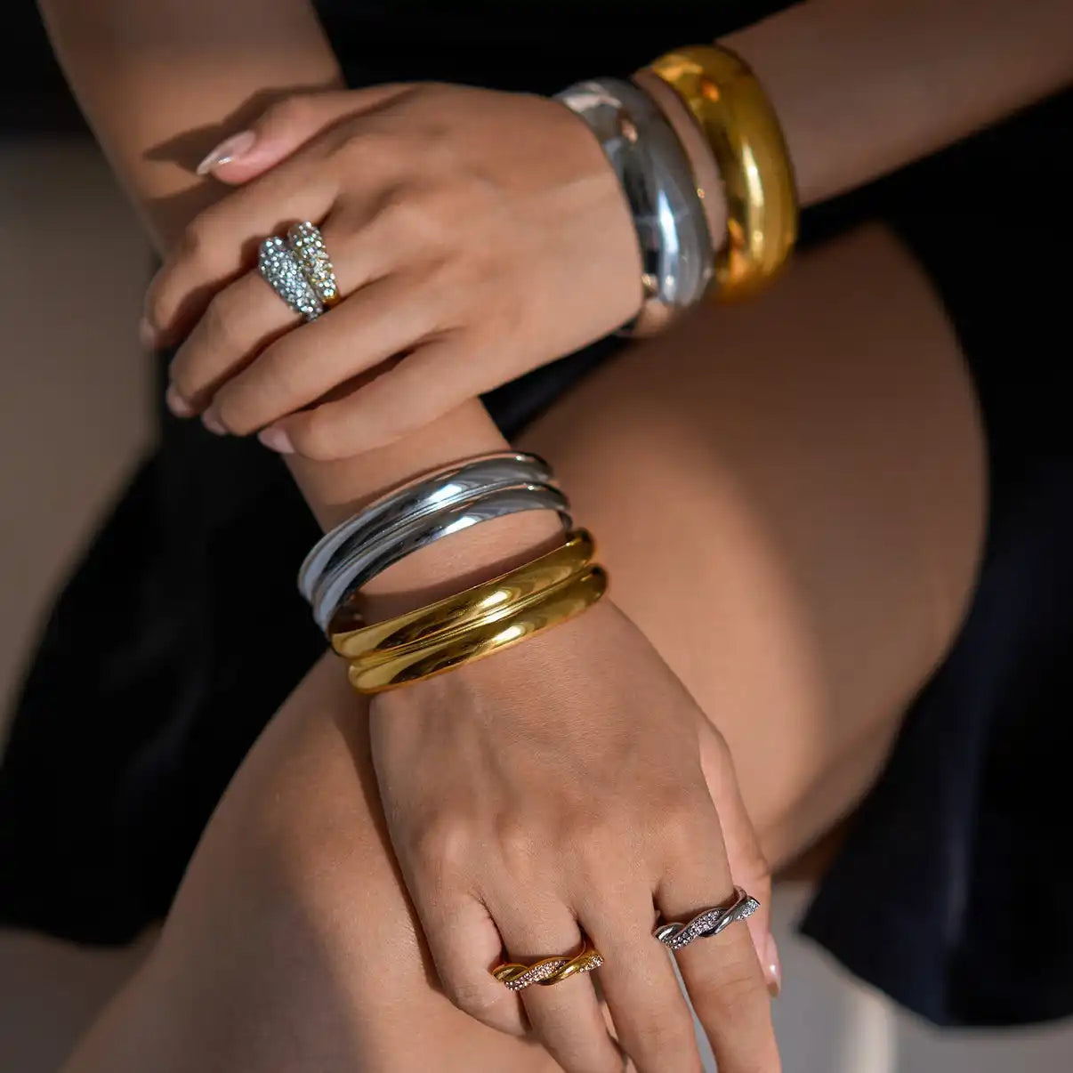 A person’s hands and arms adorned with several gold and silver bangles, and rings, one of which is a pave-set heart-shaped ring.