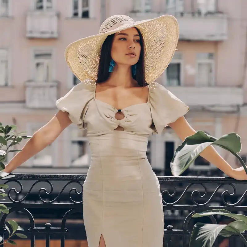 A woman in a cream-colored dress with puff sleeves, a cutout bodice, and a straw sun hat.